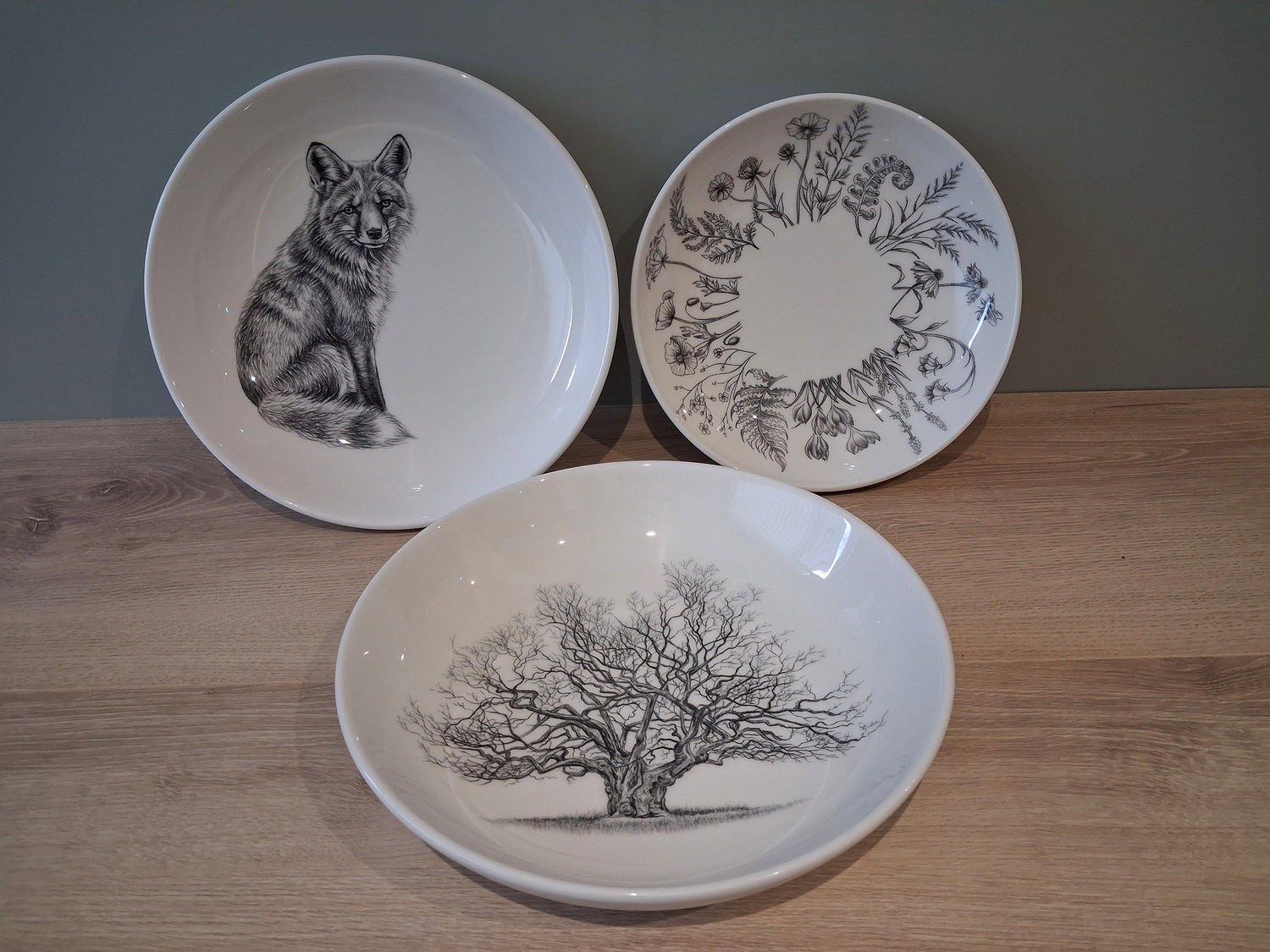 A collection of ceramic bowls featuring original drawings inspired by British wildlife. Three examples are shown including a fox, a tree and a collection of wild flowers.