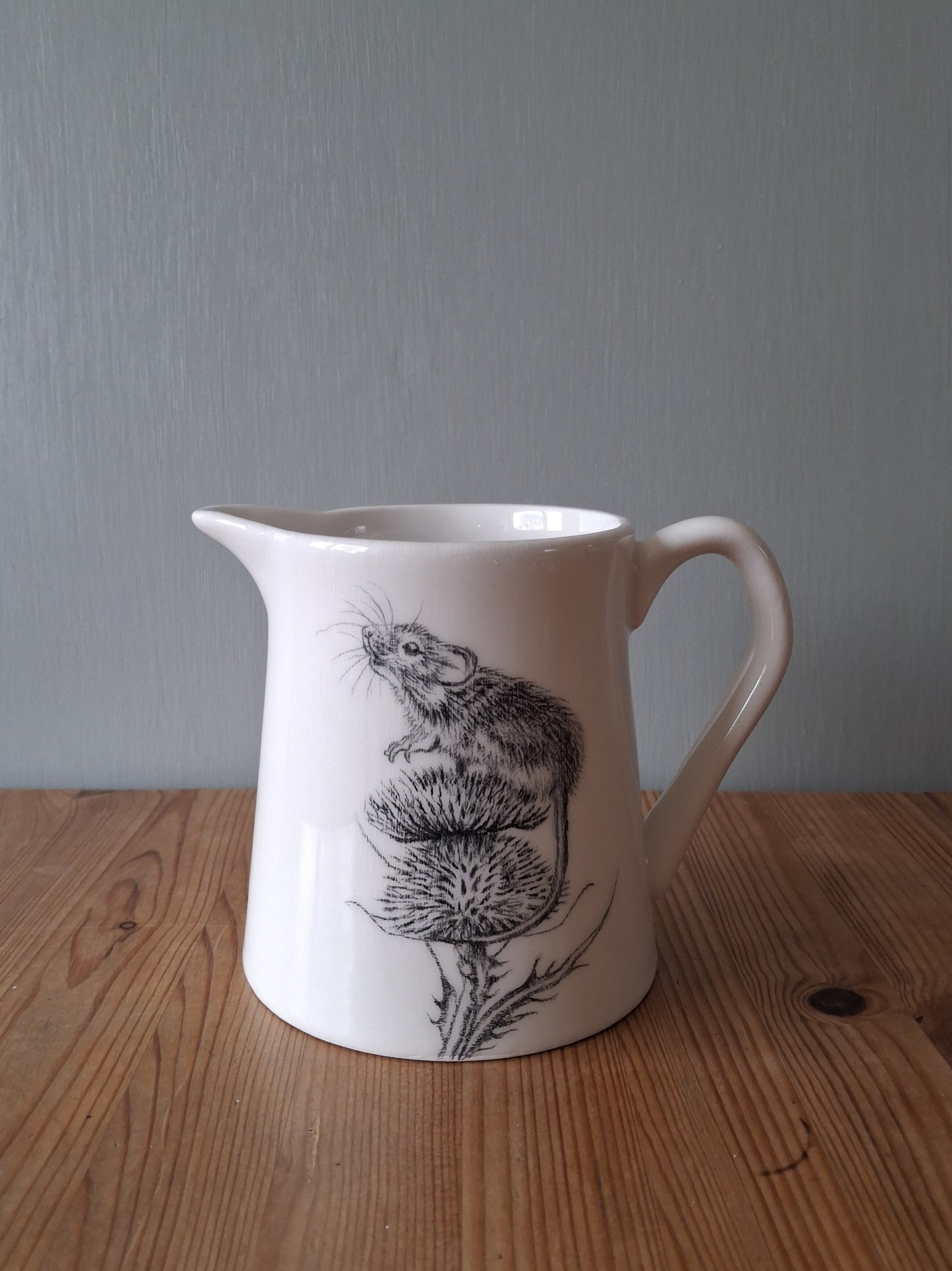 White ceramic milk jug with hand drawn image of a mouse sitting on top of a thistle.